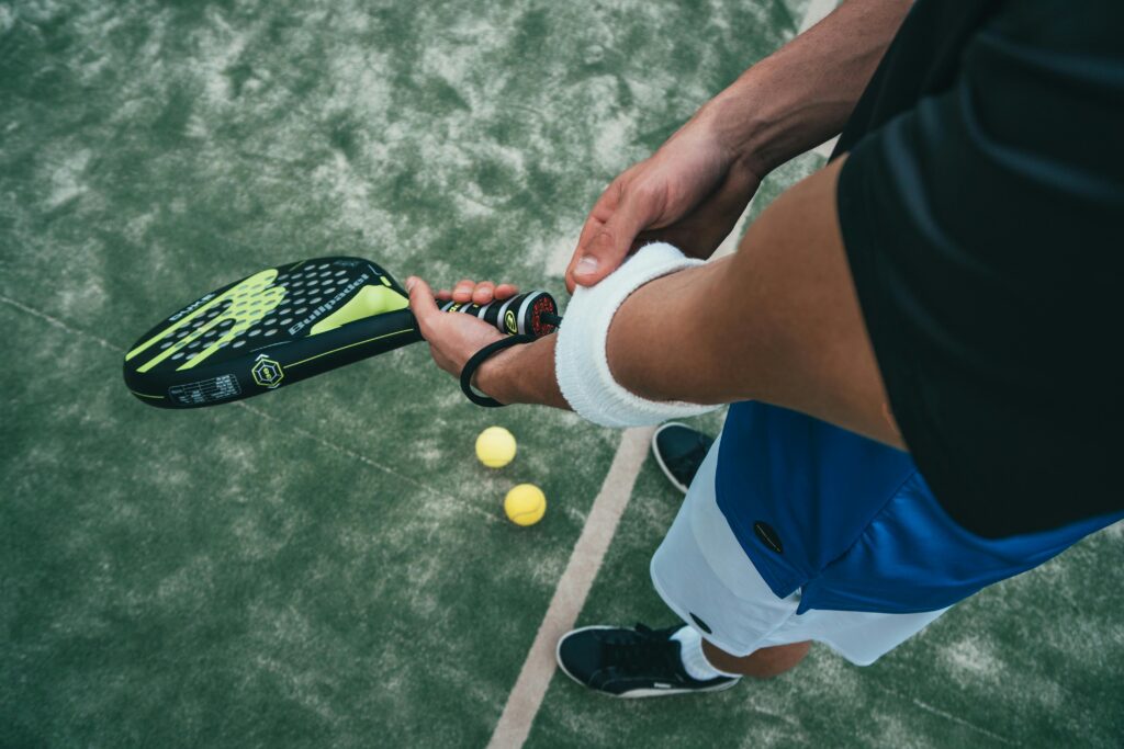 pexels-photo-1103829-1103829 Close-up of a male padel player adjusting wristband on a court. Sports action focused.